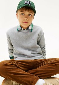 Maglione grigio in maglia waffle sopra una camicia a quadri verde e blu con colletto, abbinato a pantaloni di corduroy marroni e scarpe beige.