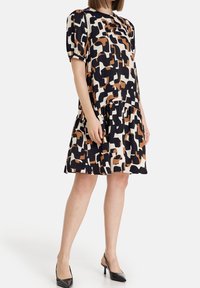 Korte mouwen jurk in een zwart, crème en bruin abstract patroon. Uitlopende zoom, lichte stof, ontspannen pasvorm en ronde halslijn.