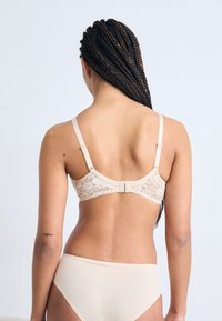 Beige bh met kant aan de achterkant, verstelbare bandjes en een haaksluiting. Soepele stof en minimalistisch ontwerp. Gecombineerd met bijpassende beige slips.