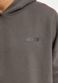 Gray hoodie made of soft fabric, featuring a hood, ribbed cuffs, and a subtle embossed "ROCAWEAR" logo in dark gray on the front.