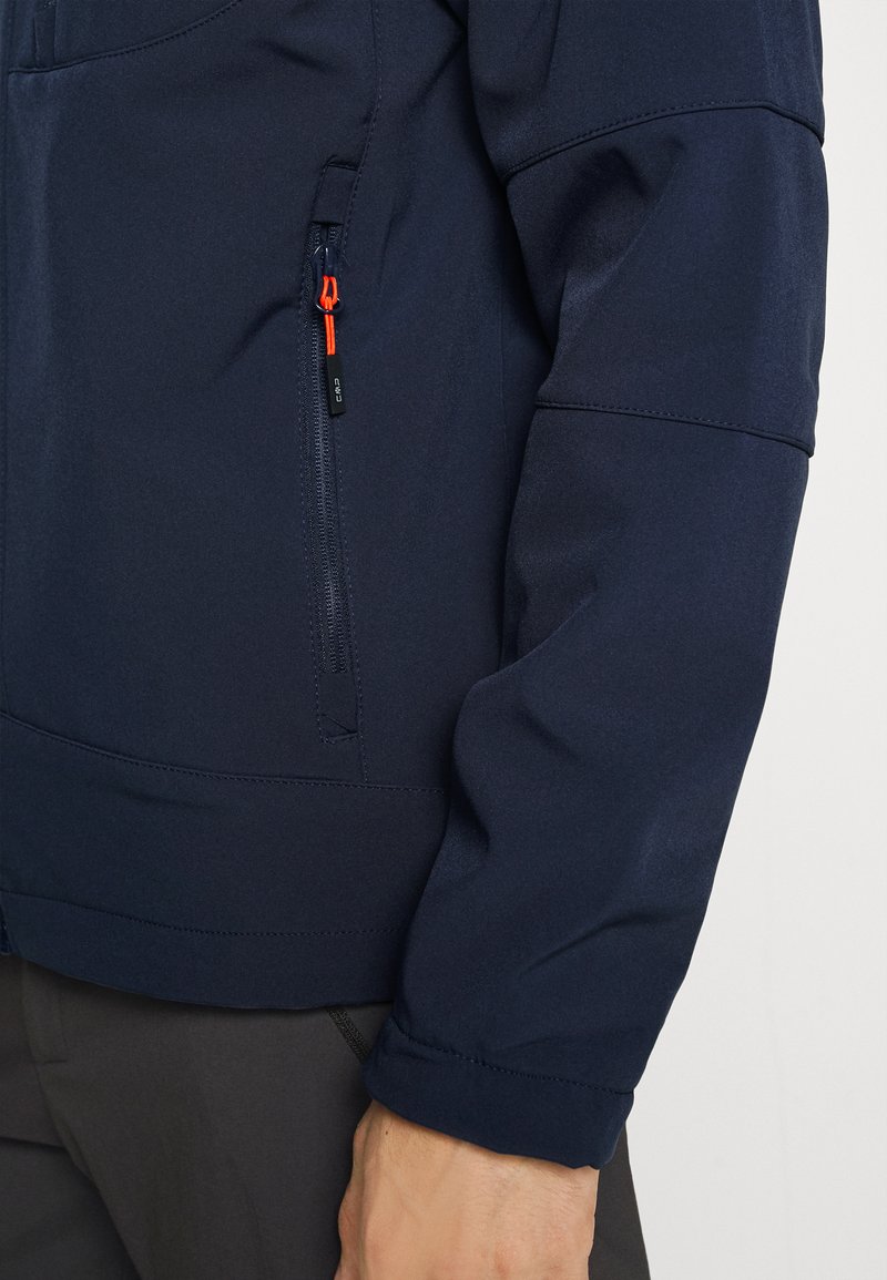 Chaqueta azul marino con un bolsillo con cremallera, que presenta una textura suave y líneas de costura sutiles. Incluye un detalle de tirador naranja en la cremallera para contraste.