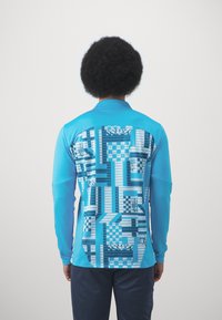 Camicia a maniche lunghe in tessuto blu brillante, con un motivo geometrico stampato in varie tonalità di blu sulla schiena.