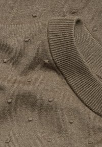 Brunstickad tröja med en texturerad yta prydd av små upphöjda prickar och en ribbad krage. Mjuk, medeltjockt tyg med en slät yta.