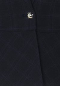 Laine navy dengan pola kotak-kotak, menampilkan detail kancing perak. Teksturnya tampak halus dengan sedikit kilau, menonjolkan desain.