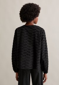 Schwarze strukturierten Jacke mit lockerer Passform, langen Ärmeln und einem einzigartigen Muster aus erhabenen horizontalen Linien. Weiches, gewebtes Material.