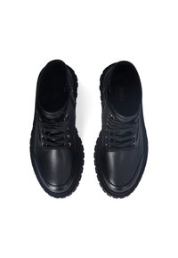Black leather shoes featuring a smooth toe cap, textured upper, metallic eyelets, and a rugged rubber sole with pronounced treads.