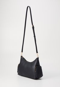 Sac à épaule noir en matériau lisse, présentant une forme courbée, une bandoulière réglable, des petites quincailleries dorées et des poches zippées sur les côtés.
