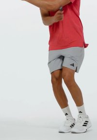 Conjunto deportivo que incluye una camiseta roja de manga corta, pantalones cortos grises con rayas negras, calcetines blancos y zapatillas blancas con detalles negros.