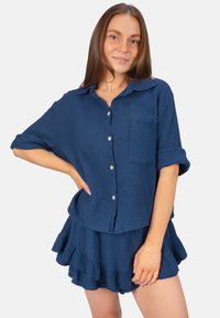 Chemise en coton texturé bleu marine avec un devant à boutons, des manches courtes et une poche poitrine, assortie à une jupe à volants.