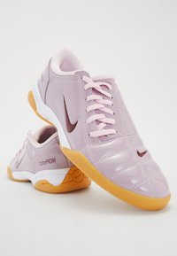 Pink patent leather athletic shoes with white accents, featuring a rounded toe, textured upper, and a rubber sole with a honey-colored grip.