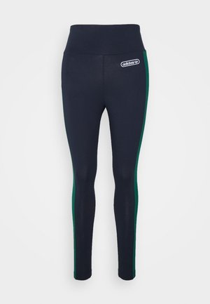 Marineblå leggings med høy midje, med grønne sidestrekker og et hvitt Adidas-logo-patch på venstre hofte. Glatt, elastisk materiale.