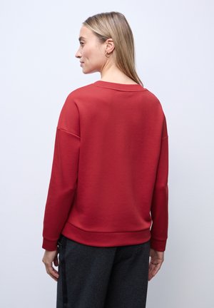 Röd sweatshirt tillverkad av mjukt tyg, med en avslappnad passform, långa ärmar och ribbade ärmmuddar. Slät textur med en enkel design.