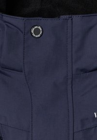 Marinblått tyg med slät yta, prytt med en cirkulär svart tryckknapp och diskreta sömdetaljer. Inga synliga mönster eller accenter.