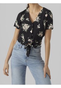 Svart blommönstrad knäppt skjorta med korta ärmar, med ett band i midjan och fina rosa och gröna blommönster. Tillsammans med ljusblå jeans.