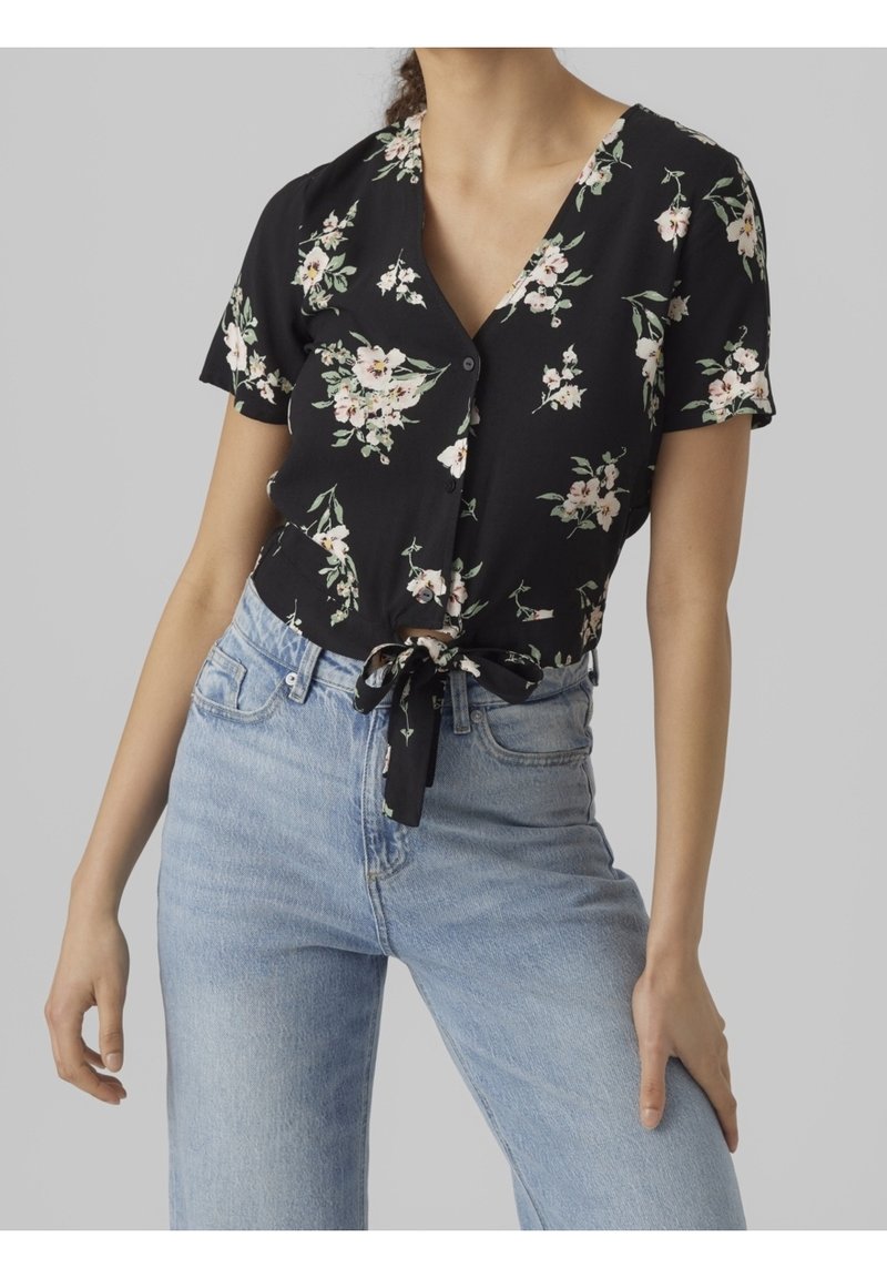 Svart blommönstrad knäppt skjorta med korta ärmar, med ett band i midjan och fina rosa och gröna blommönster. Tillsammans med ljusblå jeans.