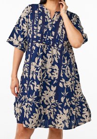 Robe florale bleu marine avec des feuilles crème, manches courtes, patte de boutonnage, panneaux en dentelle texturée et design de jupe à volants.