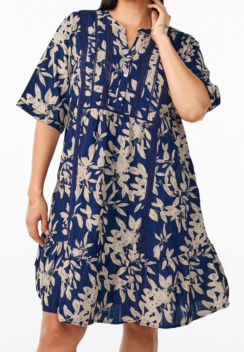 Robe florale bleu marine avec des feuilles crème, manches courtes, patte de boutonnage, panneaux en dentelle texturée et design de jupe à volants.