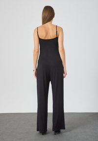 Black jumpsuit with thin straps, a fitted bodice, and wide-leg pants. Made from a smooth fabric, featuring a minimalist design.