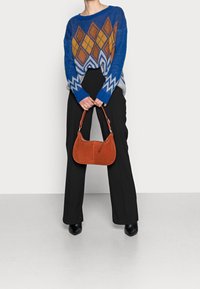 Blå, mönstrad tröja med orange diamantdesign, bärs med svarta byxor. Håller en liten, brun mockaväska med en kurvig form.
