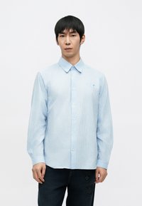 Jasnoniebieska, w paski koszula z długim rękawem, kołnierzykiem na guziki oraz małym logo na lewej piersi. Noszona z ciemnymi dżinsami.