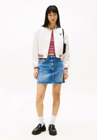 Hvid satin bomberjakke med maroon striber, rød og hvid stribet crop top, blå denimnederdel, sorte loafers og hvide ankelsokker.