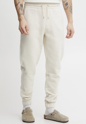 Cremfarbene Sweatpants aus weichem Stoff mit schmal zulaufendem Schnitt, elastischem Taillenbund und gerippten Bündchen. Verfügt über einen Kordelzug für eine verstellbare Passform.