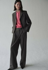 Completo grigio su misura con giacca aderente e pantaloni a gamba ampia, abbinato a una polo rosa brillante. Tessuto morbido e design strutturato.