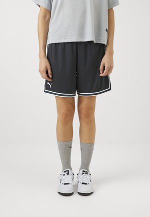 Tamsiai pilki sportiniai šortai su baltais apvadais ir Puma logotipu, derinami su pilkais kojinėmis ir baltais sportbačiais. Laisvas kirpimas, atsitiktinis dizainas.