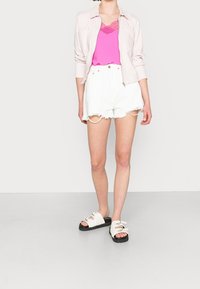Giacca rosa chiaro sopra un top in pizzo rosa brillante, abbinata a pantaloncini di jeans bianchi strappati e sandali con platfrom neri.