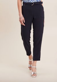 Donkerblauwe broek met een gestructureerde afwerking, taps toelopende vorm, ceintuur en zijzakken. Gecombineerd met zilveren sandaaltjes met banden.