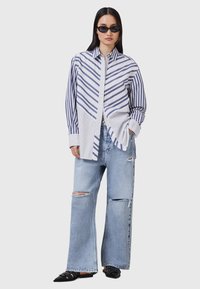 Blå og hvidstribet skjorte med knapper og lange ærmer, kombineret med slidte lyseblå brede jeans og sorte flade sko.