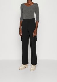 Grå långärmad tröja kombinerad med svarta skräddarsydda cargobyxor med sidofickor, buren med beige plattformsskor.