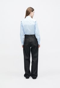 Cămașă cu dungi albastre deschise, cu mâneci lungi, asortată cu blugi din denim închis, cu talie înaltă. Cămașa are detalii cu nasturi, iar blugii au buzunare în spate.