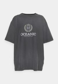 Tmavě šedé oversized tričko, bavlněný materiál, s potiskem loga se sluneční korunou a vavřínem, text "OCEANIC EXPLORATION" v bílé barvě.