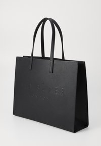 Sac fourre-tout noir en matériau synthétique texturé, avec un logo en relief à l'avant, deux longues anses et un design rectangulaire minimaliste.