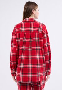 Czerwona flanelowa koszula w kratę z żółtymi, zielonymi i czarnymi liniami. Kołnierzyk na guziki i długie rękawy, zaokrąglony dół.