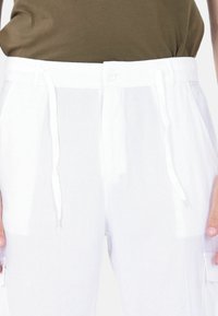 Pantaloni cargo bianchi realizzati in tessuto leggero, con vita regolabile tramite cordino, chiusura con bottone e dettagli con tasche laterali.