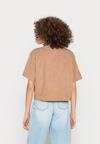 T-shirt court à manches courtes en tissu doux de couleur marron clair. Doté d'un col rond simple et d'une coupe décontractée, associé à un jean bleu clair.