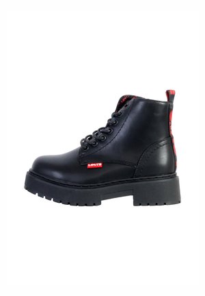 Stivale alla caviglia in pelle nera con suola spessa, caratterizzato da un marchio rosso Levi's, lacci tondi e un interno a motivo. Texture liscia nel complesso.