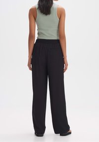 Svarta vida byxor med elastisk midja, matchade med en figurnära ljusgrön linne. Tyget verkar slätt och lätt.