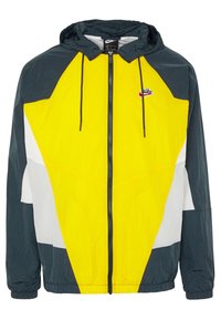 Yellow, navy, and white color-blocked windbreaker jacket with a zip closure, adjustable hood, and elastic cuffs. Features Nike logo on chest.