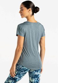 Camiseta atlética gris de manga corta, con textura suave y un corte relajado, combinada con leggings azules estampados que presentan acentos amarillos.