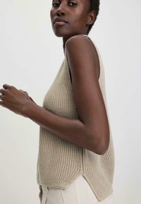 Top senza maniche lavorato a maglia in beige chiaro, caratterizzato da un motivo testurizzato, spacco laterale e una vestibilità rilassata, abbinato a pantaloni color crema.