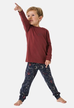 Rode langekoope t-shirt met een kleine graphic; marineblauwe pyjamabroek met kleurrijke hemelse patronen. Kind in een speelse pose.