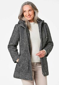 Grijs jassen met een vijgenpatroon en capuchon, grijze accenten en zijzakken, gedragen over een crèmekleurige gebreide trui. Lichtgewicht stof, middellange ontwerp.