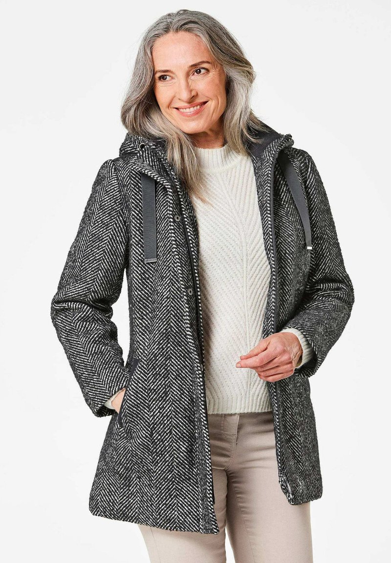 Grijs jassen met een vijgenpatroon en capuchon, grijze accenten en zijzakken, gedragen over een crèmekleurige gebreide trui. Lichtgewicht stof, middellange ontwerp.