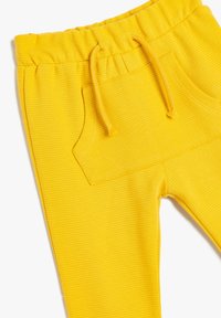 Gule ribbede joggingbukser med elastisk talje, snøret og en frontlomme. Glat tekstur med en tætsiddende design.