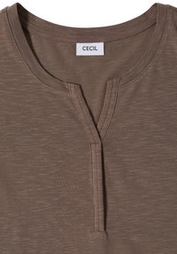 Chemise marron à manches courtes avec un col rond fendu et une étiquette de marque "CECIL" visible à l'intérieur du col.