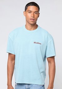 Camiseta de algodón azul claro con un corte relajado, cuello redondo y mangas cortas. Presenta un pequeño logo en rojo oscuro de "Dickies" en el pecho.