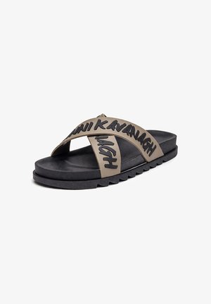 Schwarze Slide-Sandale mit dicken beige gekreuzten Riemen mit dem Schriftzug „KAVANAGH“ und einer profilierten Sohle für besseren Halt.